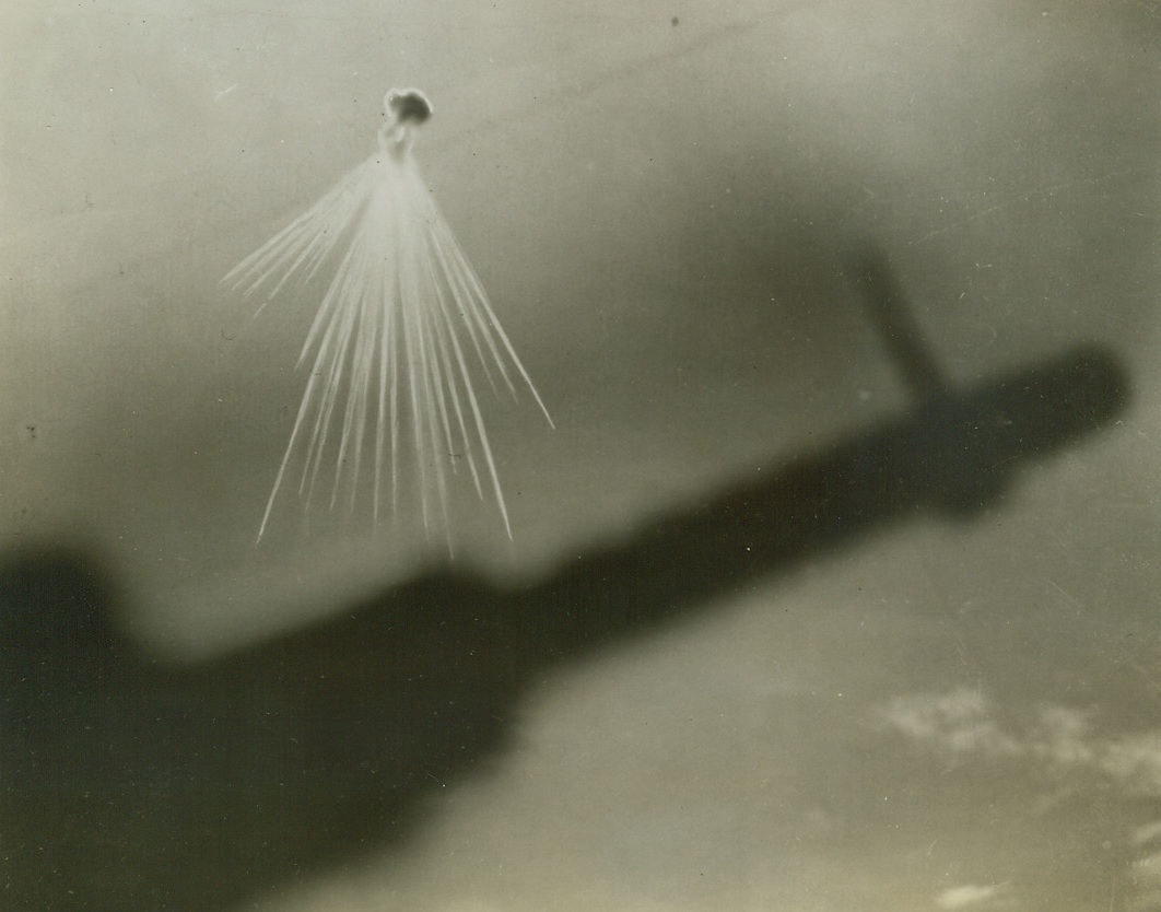 Jap Aerial Incendiary Bomb, 12/24/1943. Marshall Islands – The incendiary fingers of an aerial phosphorous bomb spray out as the Japs attempt to break up formations of 7th Air Force Liberator Bombers, which are striking daily at Jap bases in the Marshalls. The bomb burst was photographed from the waist window of a Liberator, with the silhouette of the bomber’s .50-calibre waist gun in foreground. Credit: 7th Army Air Force photo from ACME;