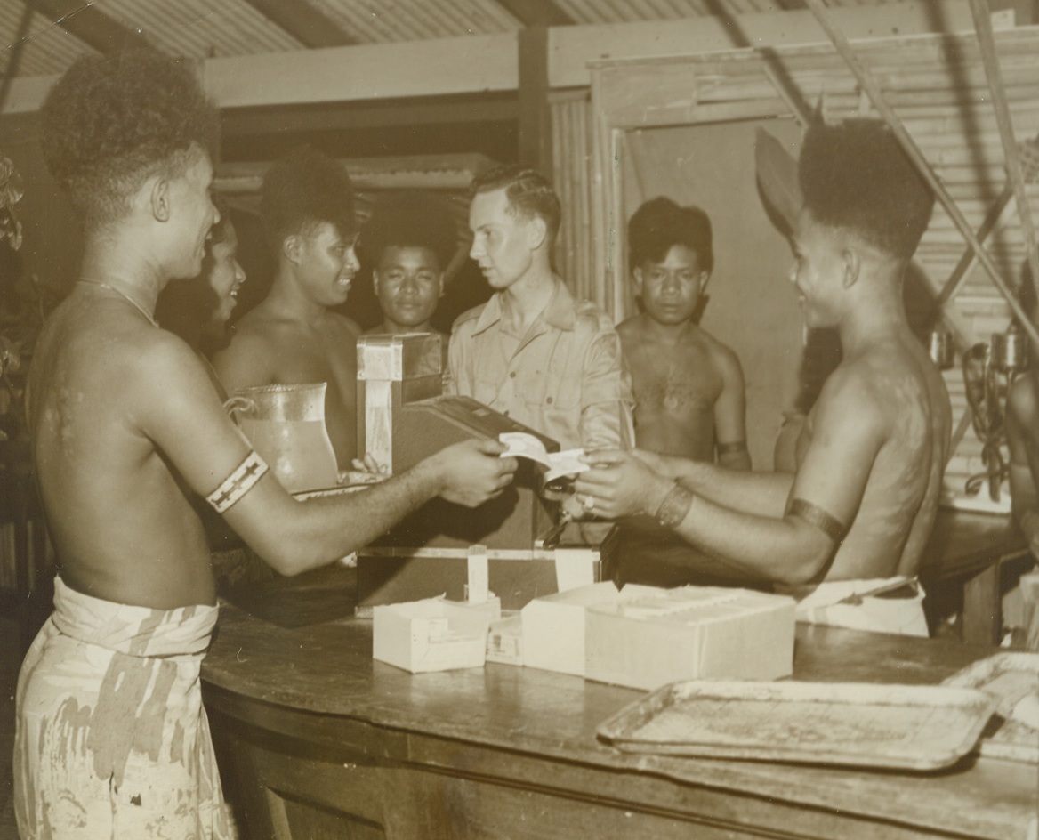 New Guinea Counter Man, 12/13/1943. New Guinea – Easily taking to the complexities of modern life, Fuzzy-Wuzzies, natives of New Guinea, handle the jobs of cashier and waiters with ease. Gudu Udau works the cash register while other natives wait for change. The picturesque Fuzzy-Wuzzies also help carry supplies, wounded and ammunition through the jungle. Credit: ACME;