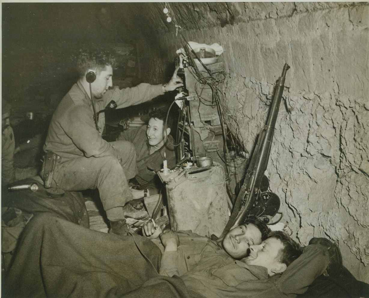 Entertainment Courtesy A. Hitler, 12/19/1943. MIGNANO, ITALY -- A German radio, found on a battlefield, provides entertainment for these American soldiers as they "bivouac" in an old wine cellar (minus the wine) in Mignano, after their battle for the Italian town. At the switchboard is Pfc. Howard L. Saddler of Canton, Ohio. Pvt. Theodore Zembuiski of Albany, NY, lounges in background, while (left to right) Pvt. Thomas G. Cross of Buffalo Gap, Texas, and Pfc. Norman S. Roy of Baltimore, MD., lie in foreground. Credit: (ACME);