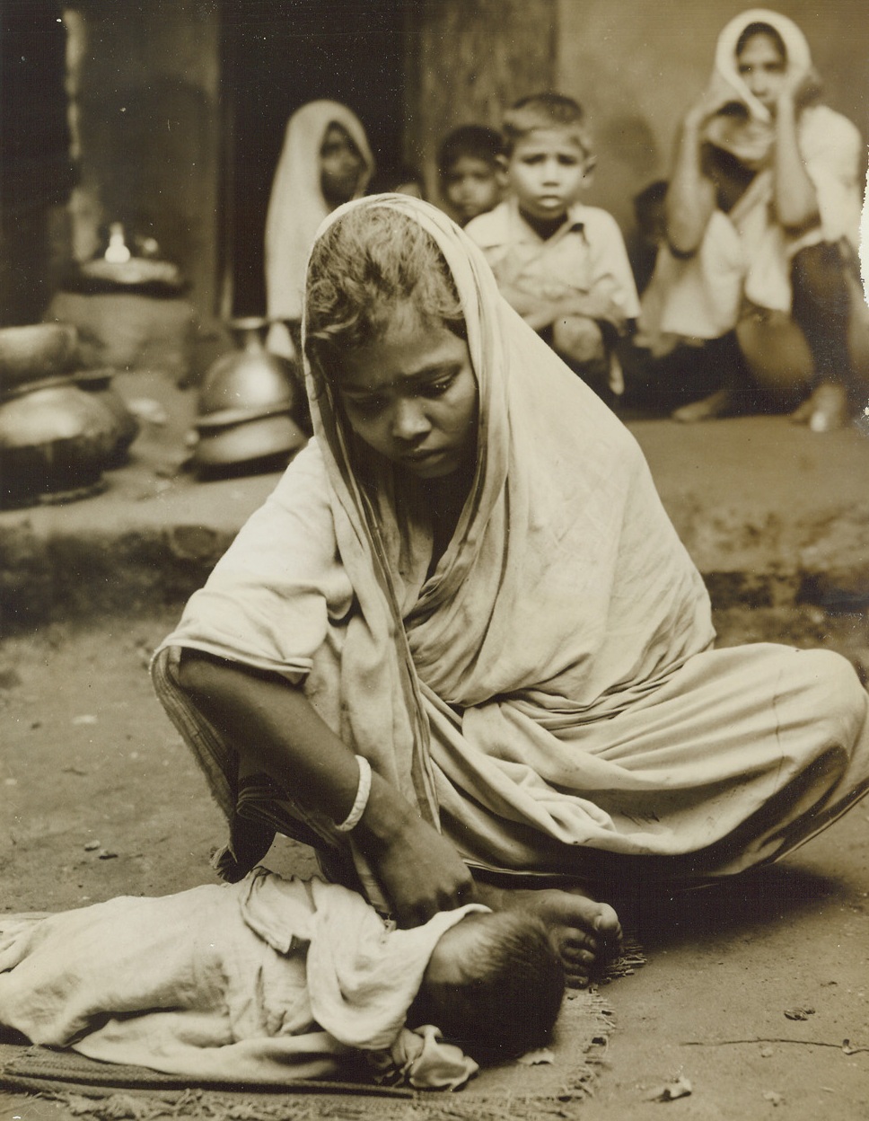 Famine in India, 12/17/1943. By last week, an estimated 1,000,000 persons had died of starvation in India and, although the British government reportedly has the situation under control, that number will undoubtedly be raised before the final, tragic count is taken.  Just released, these startling pictures were taken in Calcutta at the peak of India’s famine in late October when a homeless army of 100,000 roamed the city, dying in the streets.  New York BureauA young Indian mother covers the body of her baby who has just drawn a last weak breath.  Now the homeless woman must wait for the corpse removal squad that picks up the bodies of children who starved to death. Credit Line (ACME);