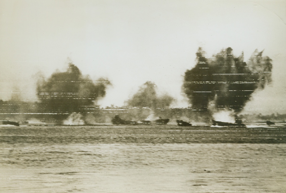 Bombs Fall on the Invaders, 12/18/1943. Arawe, New Britain - Clouds of thick, black smoke rise from the water as Japanese planes bomb and strafe American landing craft during the yank invasion of New Britain, at Arawe.  Miraculously, no ships were hit during the bombing.  Only two LCV’s were lost in the entire operation. Credit (U.S. Signal Corps Telephoto - ACME);