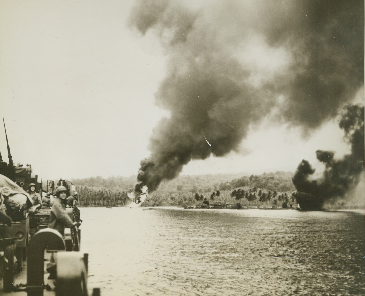 Enemy Inning, 12/28/1943. Guadalcanal, S.I. - - Jap bombers provided this sobering welcome for a U.S. Navy warship sailing into port at Guadalcanal.  Flames still burn brightly from hits registered by the enemy who left a short while before the ship entered the port.  Gun crews aboard ship stand by at their posts, ready to greet the - - - Japanese, when and if they return.Credit (U.S. Navy photo from ACME);