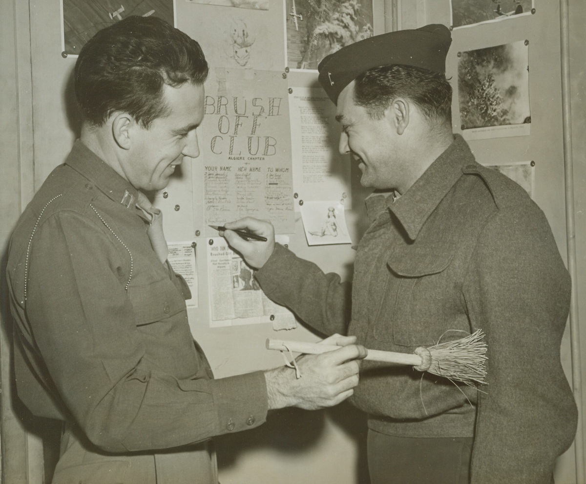 The End of Romance, 12/29/1943. Algiers -- Lt. Russell Brickell, of Fort Worth, Texas, signs his name to the ever-expanding roster of the Algiers chapter of the “Brush-Off Club” as charter member Capt. Howard Hammersley Jr. literally brushes his buddy off. Membership is open only to those overseas fighters who lady loves have ditched them. Capt. Hammersley hails from Roanoke, Virginia. Credit: ACME photo by Charles Seawood for War Pool;