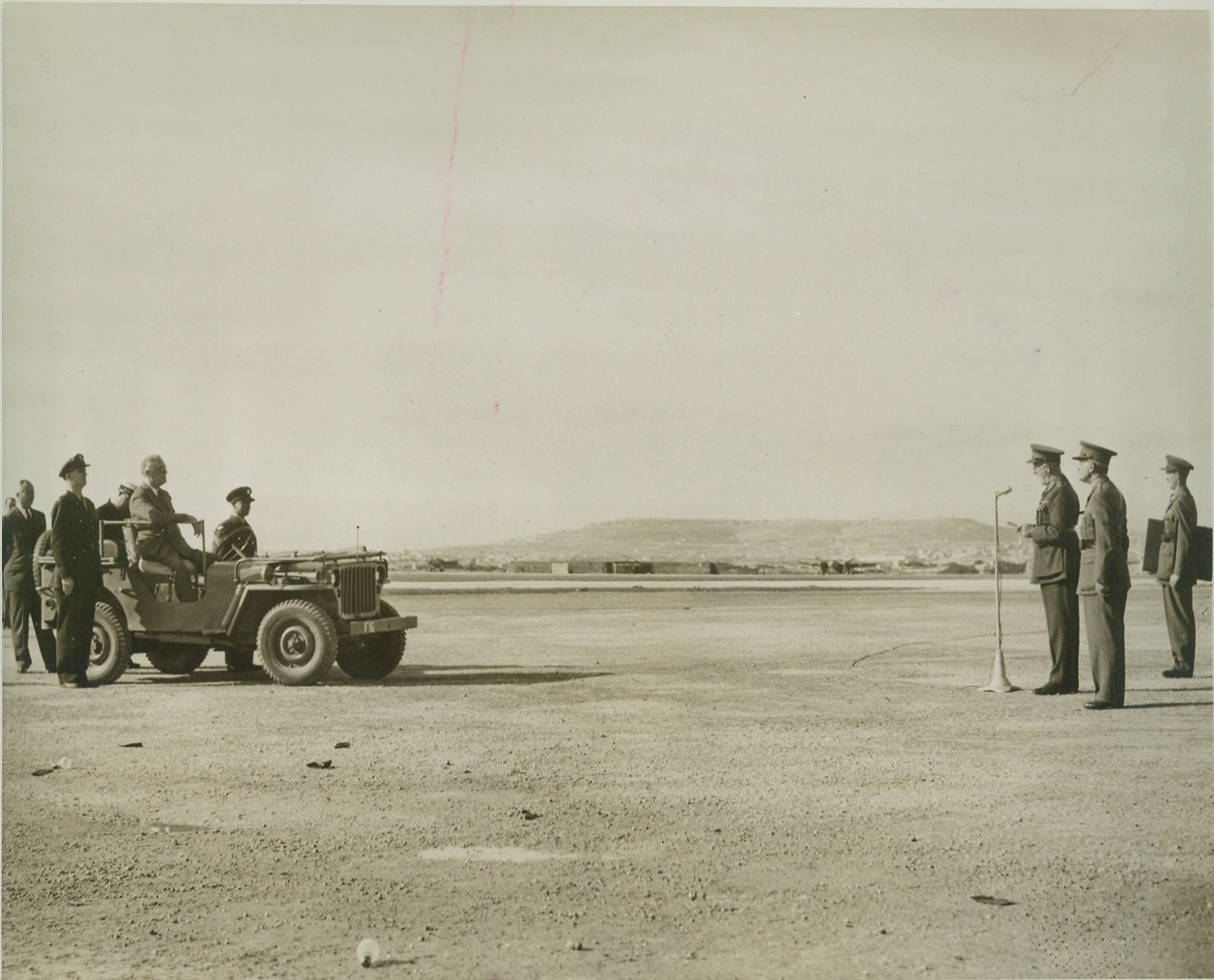 Lord Gort Accepts Scroll from President, 12/14/1943. MALTA – Field Marshal Lord Gort, (at microphone in group at right), as he made a speech of acceptance for a scroll presented to the people of Malta on behalf of the people of the U.S., and expressing American admiration for the courage and fortitude of the Maltese. Just before this photo was taken, the scroll was presented to Lord Gort by President Franklin D. Roosevelt, (seated in Jeep, at left). Standing near the rear wheel of the Jeep, (left foreground), is Major John Boettiger, the President’s son-in-law, who actually handed the scroll to Lord Gort, during the recent ceremony. Credit: (OWI Photo from ACME);