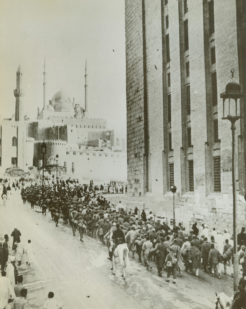 Axis Prisoners of British Reach Cairo, 1/2/1942. Cairo, Egypt – A column of prisoners, captured in Libya during the current British offensive, as they neared the massive walls of the Citadel of Cairo, built by Saladin, showing the landmark of the Mohamed Al Mosque above, and the Mosque of Sultan Hassan (right).  Note crowd of curious natives at left.  They are being escorted by Egyptian mounted police (white horses). Credit line (ACME;