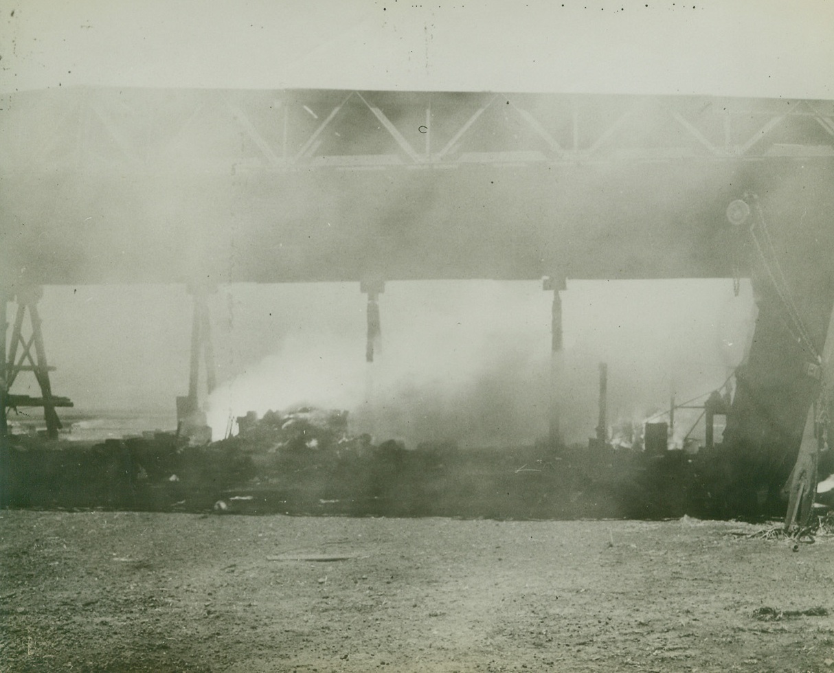 BATTLE RAGING IN THE SOLOMONS, 10/15/1942. United States Forces are striving to prevent the Japanese from landing reinforcements on Guadalcanal. The above photo just released by the US Navy shows-smoke and flame shrouding the remains of a hangar at Guadalcanal after a heavy Jap attack. Despite heavy losses in bombers, fighters and ships the enemy is increasing it’s pressure on American positions.  Credit Line Navy Official Photo from ACME);