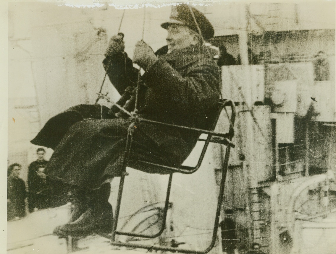 ADMIRAL CHANGES SHIP IN MID-STREAM, 10/9/1942. Rear Admiral R. L. Burnett, commander of the escorting forces convoying the largest Allied merchant fleet to a Russian arctic port, is seated in a slung chair as he transfers from the cruiser flagship H. M. S. Scylla to a destroyer following a four-day torpedo plane and U-Boat attack by Axis forces. The cruiser was used to accommodate survivors of sunken ships. Admiral Burnett saw the convoy to Russia from the destroyer. (Passed by censors.) Credit: ACME;