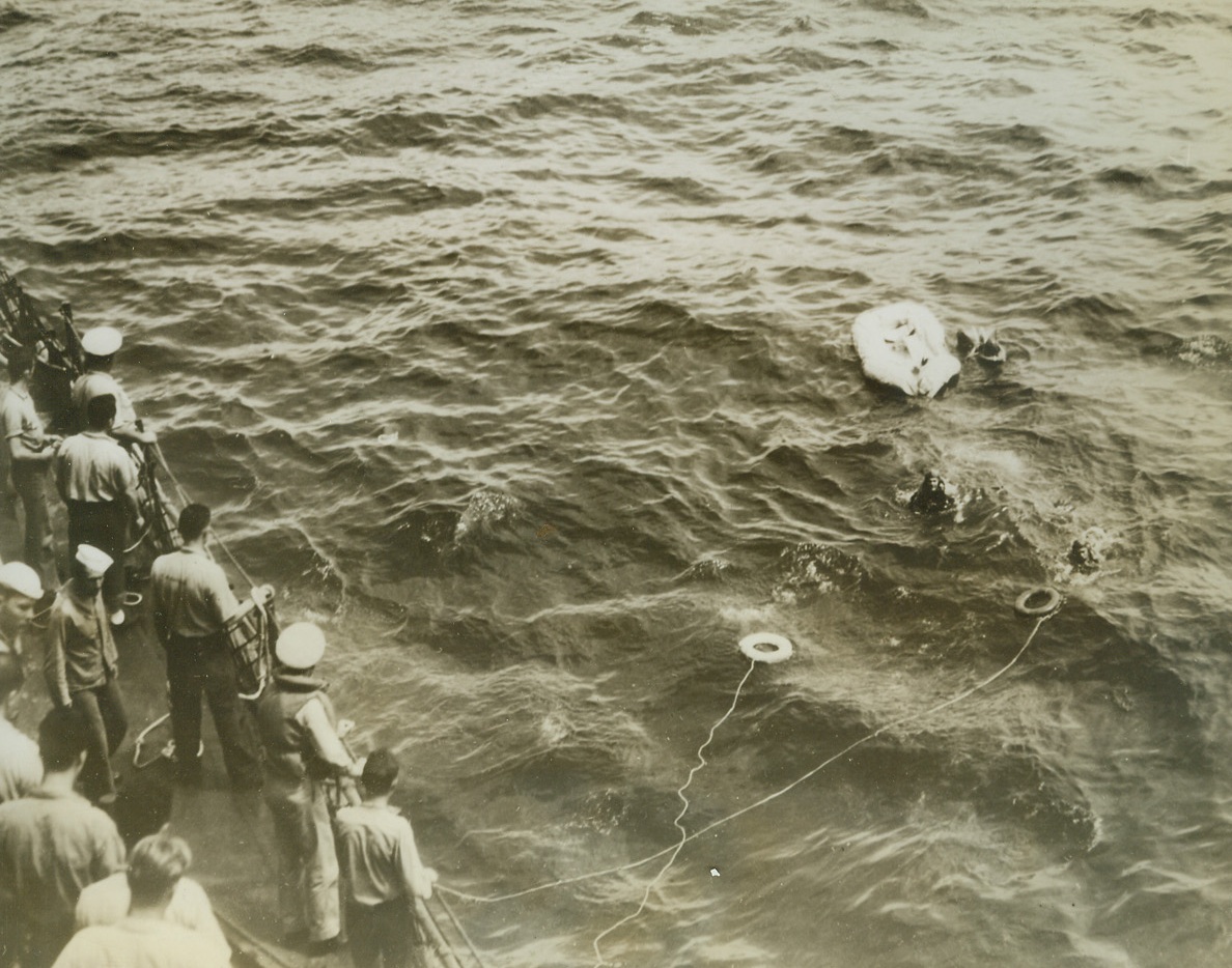 SAVED AFTER JAPANESE ATTACK, 10/23/1942. Three U.S. airmen, their plane shot down in the Solomon Islands area by Japanese, took to their rubber “doughnut” until rescued by the ship at left. The man at the extreme right is just reaching for the life preserver, while another treads water and the third appears to be hanging onto a piece of equipment by the rubber boat. Credit: U.S. NAVY PHOTO FROM ACME.;