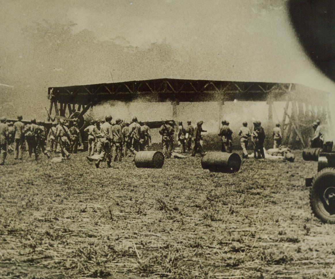 U.S. MARINES FIGHT FIRE IN BOMBED HANGAR, 10/21/1942. This Photo, which has just been released and which is from an Official U.S. Marine Corps newsreel, shows American Marines on Guadalcanal Island fighting fire and rescuing equipment from a hangar on Henderson Field, set afire during a recent attack by Japanese bombers. Note drums of fuel, (foreground), salvaged from the blaze.  Credit: U.S. MARINE CORPS PHOTO FROM ACME.;