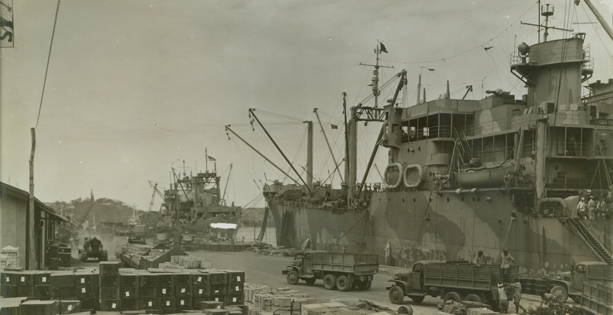 Supply Ships for the Solomons Load Up, 10/2/1942. South Pacific Port – Tons of foodstuffs, motors, oil and tractors wait on the dock of a South Pacific Port to be loaded for shipment to the Solomon islands, where they will supply U.S. Marine and Nay forces entrenched and ready for new assaults on Jap bases. Credit line (ACME);