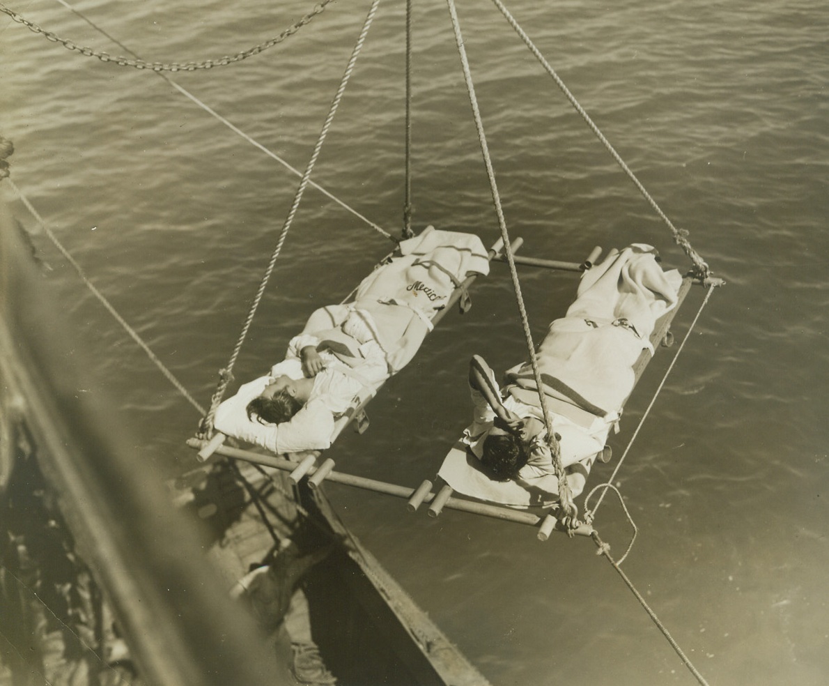 Solomon Wounded Arrive to Safety, 10/2/1942. South Pacific Port – A special stretcher-bearing crane (above) transfers wounded men from transport to shore boat to shore at a South Pacific port, where they will receive further medical aid.  The men took part in the battle of the Solomons. Credit line (ACME);