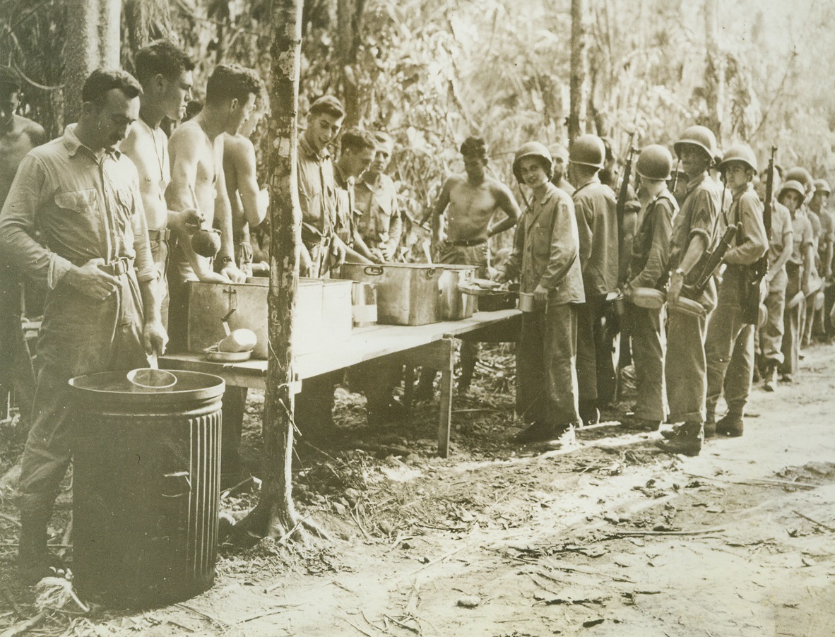 Chow on Guadalcanal, 10/23/1942. Solomon Islands – U.S. Marines who are battling to hold strategic American positions on Guadalcanal island line up for chow served cafeteria style in the island’s jungle.  Picture was made shortly after U.S. troops had blasted the Japs out of several of their positions in the strategic Solomons. Official Marine Corps photo from ACME;