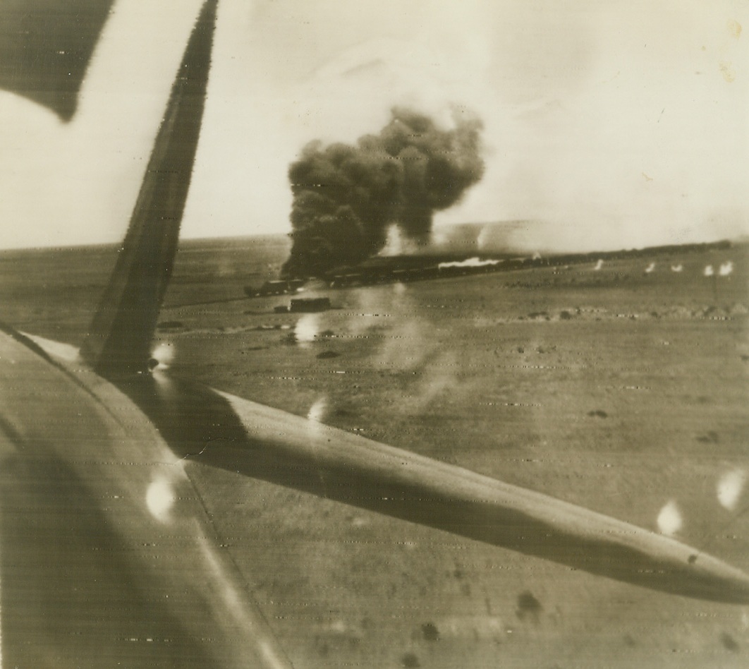 Axis Desert Supply Train Shattered, 10/16/1942. This remarkable picture of an enemy supply train ablaze after an attack by long range RAF fighters and South African Air Force light bombers was taken backward over the tail of one of the attacking planes.  An ammunition car was blown to pieces and the locomotive set afire by low flying fighters which raked the train with cannon fire.  Twenty six cars were left shattered.  Photo was flashed to New York from Cairo today by radio. Credit (ACME radio photo);