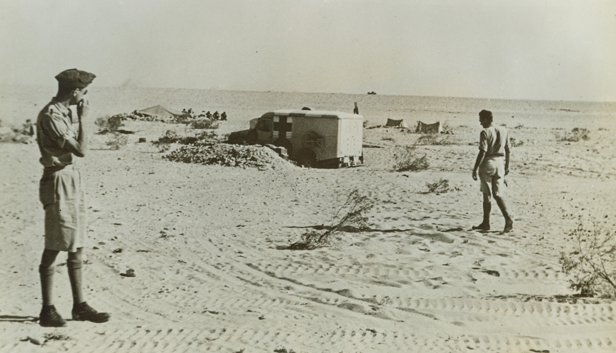 First Aid in North Africa, 10/25/1942. North Africa—A regimental aid post, a med unit with Allied forces, is parked on the front line where it will do the most good in the desert war. Frederick W. Hoeing, (left), of Rochester, N.Y., is a volunteer ambulance driver. In the far background on a tank patrol. Credit: ACME.;