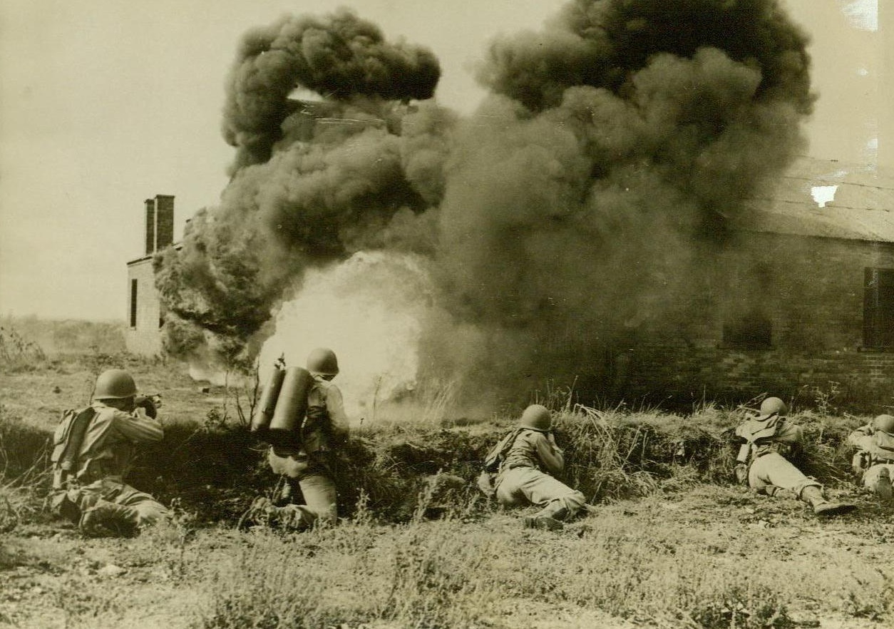 Uncle Sam's fighters holding maneuvers in England, 10/13/1942. Field, N. J, Keeps his flame-thrower pouring liquid fire at an “enemy” strongpoint. His fellow soldiers keep their tommy guns chattering. These men- Uncle Sam’s fighters holding maneuvers in England- were given intensive training in modern warfare and stressed, for the first time in maneuvers in Britain- the use of Chemicals as offensive and defensive weapons.  Credit Line (Acme) 10/13/42;