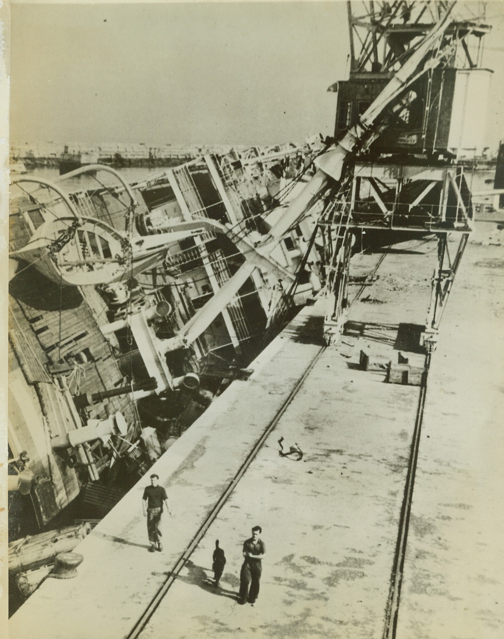 ON HER SIDE, 11/25/1942. MOROCCO – A capsized merchantman careens against the quay in Casablanca harbor after defenders of the seaport were defeated by American forces. Latest dispatches from the North American front indicate progress in the British drive on Bizerte and Tunis. Credit: ACME;