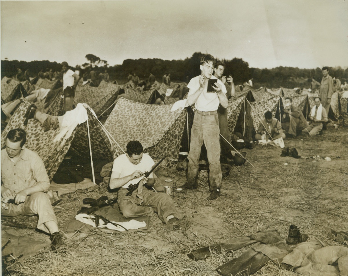 Leisure Time, 11/5/1942. NEW RIVER, N.C. - Even their leisure time must be devoted to countless necessary tasks. In bivouac after landing operations, these Marines sit before their camouflaged pup tents and clean their rifles to keep them in working order while their buddies shave. This is part of the training the men receive at the U.S. Marine Base at New River. Credit: (ACME);