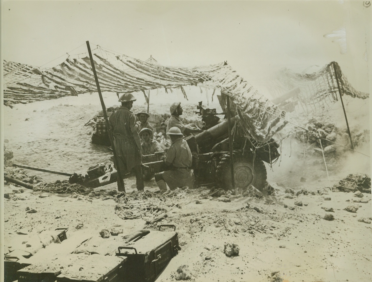 DESERT DEATH, 11/6/1942. WESTERN DESERT – Under a netting that camouflages the heavy cannon from enemy aircraft, a Greek Army crew fires a shell into an enemy aircraft position in the Western Desert. Latest reports indicate the Axis forces are being crushed by the fury of the United Nations dive to push Rommel’s army out of Africa. Credit: ACME;