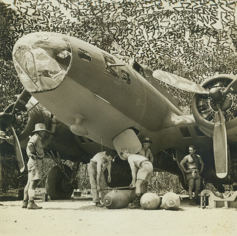 Packing the Eggs, 11/1/1942. Port Moresby – American soldiers load quarter-ton bombs into a B-17 bomber upon its return from a mission.  A zig-zag camouflage net hides the plane from the air. Credit line (ACME);