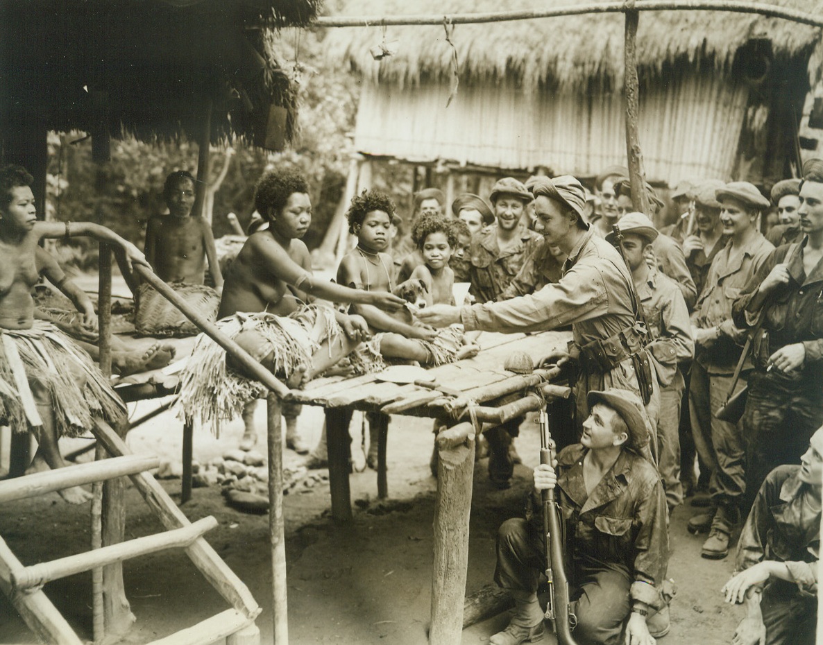 Billet Doux?, 11/13/1942. New Guinea – U.S. soldiers crowd close to a jungle hut where kinky-haired native belles line up on the front porch to inspect their khaki-clad visitors, in New Guinea. Credit line (ACME);