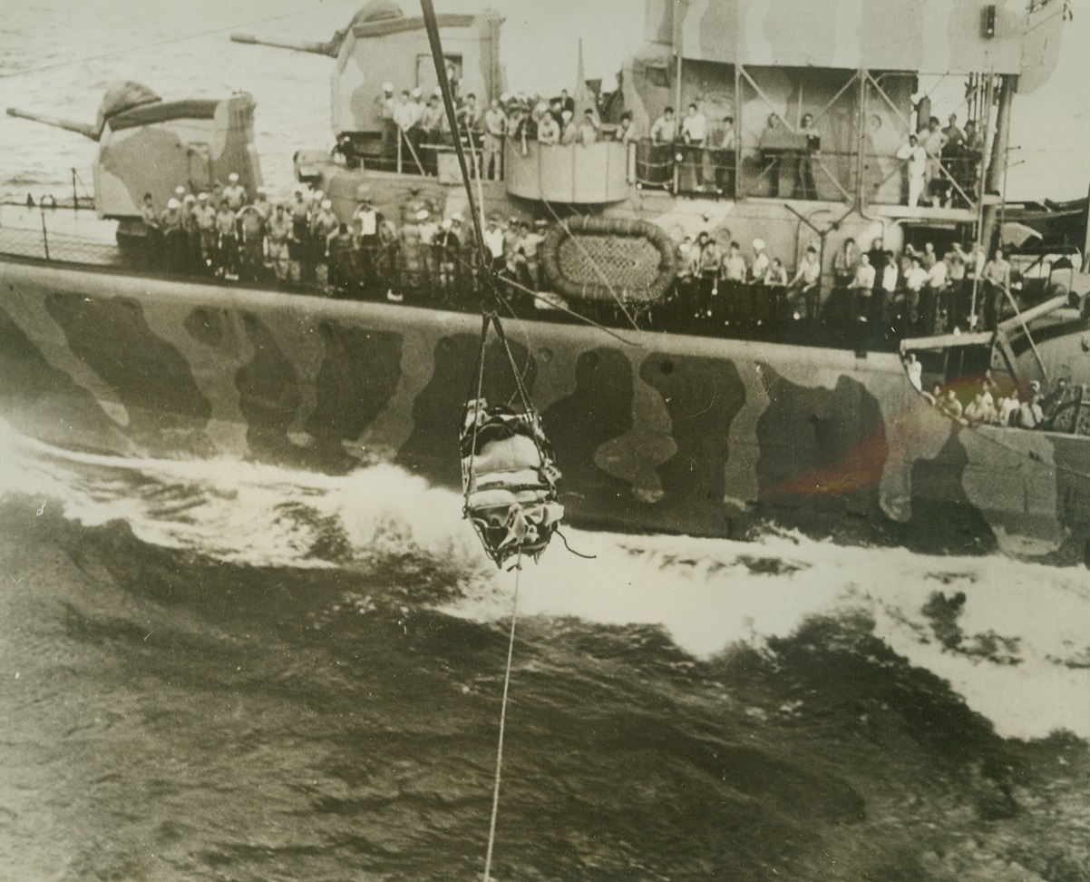 Transfer At Sea, 11/10/1942. Somewhere in the Pacific – Securely strapped in a metal basket, Sgt. R.P. Anderson, U.S. Army Airman, is transferred from a U.S. destroyer, (background), to an aircraft carrier for hospital treatment.  Anderson, member of a flying fortress crew, and six companions were rescued by the destroyer after spending seven days on a raft in the Pacific, following a crash landing. Credit line (U.S. Navy official photo);