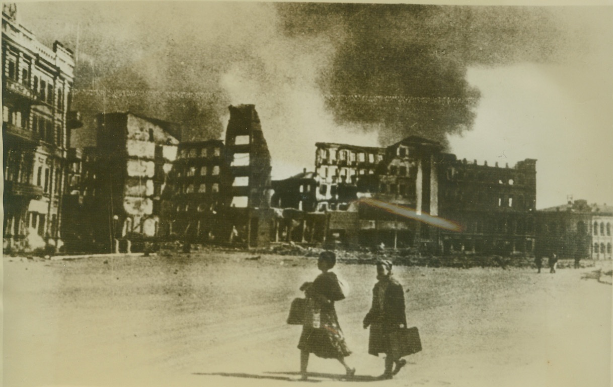 First Glimpse Inside Stalingrad, 12/14/1942. Stalingrad, Russia – For many months a lack of photographers shrouded the bloody battle for Stalingrad in half-mystery. This is one of the first pictures to be issued showing the inside of the besieged Russian stronghold with its blazing, debris-strewn streets. Russian women are shown carrying supplies to grim defenders who now have reversed their roles and are attacking the Nazis. Credit: (ACME);