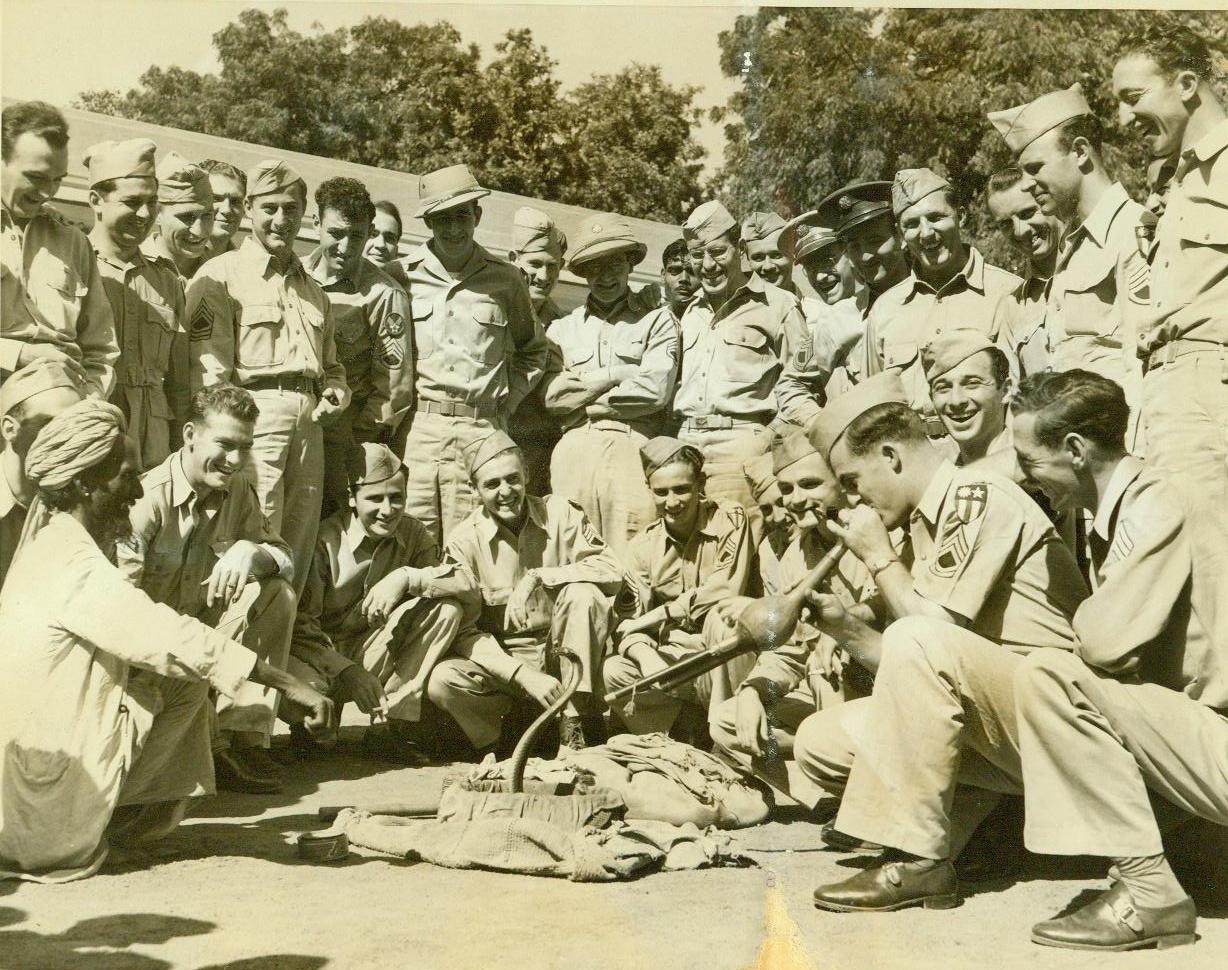 ”MUSIC HATH CHARMS -!”, 12/17/1942. INDIA – A crowd of American soldiers stationed in India, watch a buddy, Sgt. John Stafford, of West Point, Miss., (in front, second from right), tackle the ticklish job of charming a hooded cobra. The native snake charmer, (left, front), stands by in case Johnny runs out of wind. Credit: ACME;