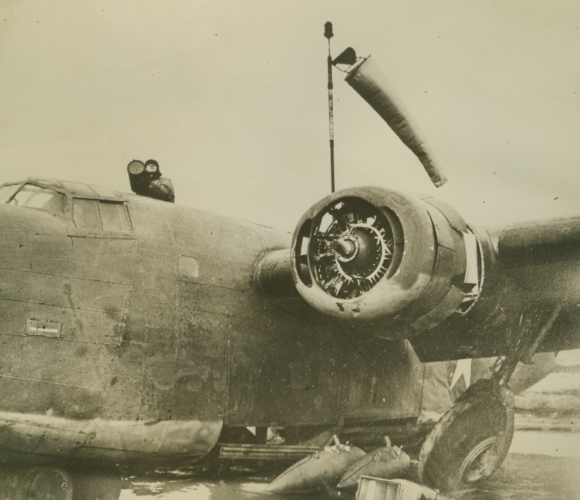 JUNKED BOMBER SERVES AS ALEUTIAN CONTROL TOWER, 12/18/1942. ALEUTIANS—Salvaged after a crash in the Aleutians, this B-24 bomber now serves as a control tower for the airfield where Lt. Col. John Chennault, son of Brig. General Claire L. Chennault, leader of the Flying Tigers, heads his own group of sky-fighters. The control man stands where a gun turret formerly was, and the wind indicator air sock waves from a staff amidships. Credit: Acme;
