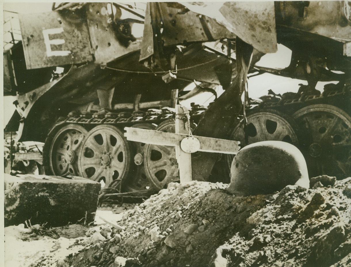 “E” FOR “EXTERMINATION”, 12/2/1942. WESTERN DESERT – The “E” (upper left in photo) painted on this shattered German tank was put there by Allied sappers to signify that it has been “exterminated” completely and that it contains no dangerous explosive charges to act as a booby trap against the Allies. The grave marked with a cross made of box wood marks the “extermination” of a member of the Nazi tank crew. Note dog tag hanging from cross and German helmet. Rommel’s Axis forces, after fleeing from Egypt, are being menaced from front and rear by United Nation’s columns and may be forced into a “Dunkirk” evacuation near Tripoli. (Passed by censors.) Credit: ACME;