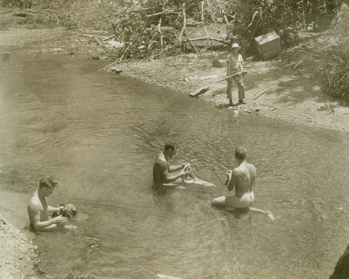 Bath Tub, Wash Tub, 12/30/1942. SOMEWHERE IN NEW GUINEA—American soldiers press this body of water into double service—as a bath tub and a washtub.  They launder their clothes and themselves as a watchful guard stands on shore to spot any unwanted visitors.  Latest reports from New Guinea indicate that two expanding Allied wedges are threatening to isolate Jap forces on Buna beachhead.Passed By CensorCredit:  ACME;