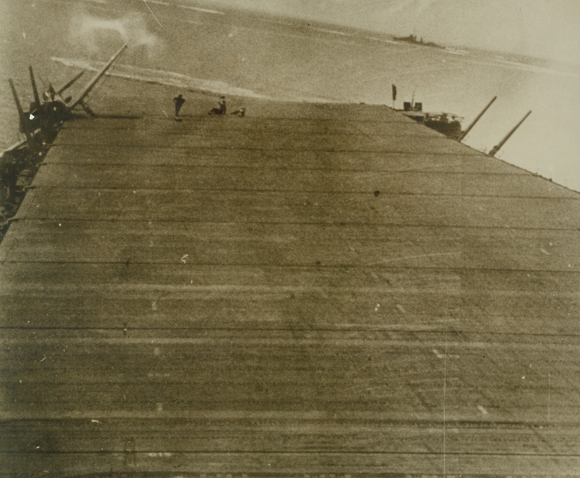 MAN-MADE EARTHQUAKE, 12/22/1942. An exploding Jap Aerial bomb which exploded eastern of this U.S. aircraft carrier, (white ring on surface of water, in background makes where explosion occurred), tossed this fighter plane overside into gun emplacement (left in photo), and knocked two crew members down, (center). Photo, which was taken during recent action in the South Pacific, was released in New York today. No American ship, which took part in the battle of which the above action was a part, was more than slightly damaged. Picture was taken from an official newsreel. Credit: U.S. NAVY PHOTO FROM ACME.;