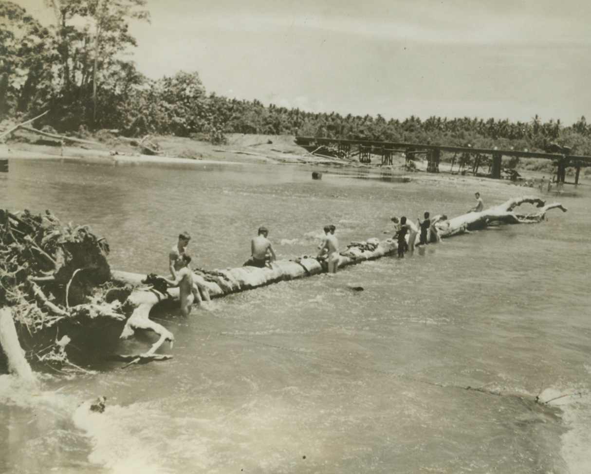 Same Old Sport – New Spot, 12/22/1942. Guadalcanal – American soldiers and Marines, along with two native guides, combine the job of washing their clothes with the sport of swimming, in the Lunga river on Guadalcanal island in the Solomons.  A huge fallen tree is used both as a washboard and a seat for sun bathing.  Credit line (U.S. Marine Corps from ACME);