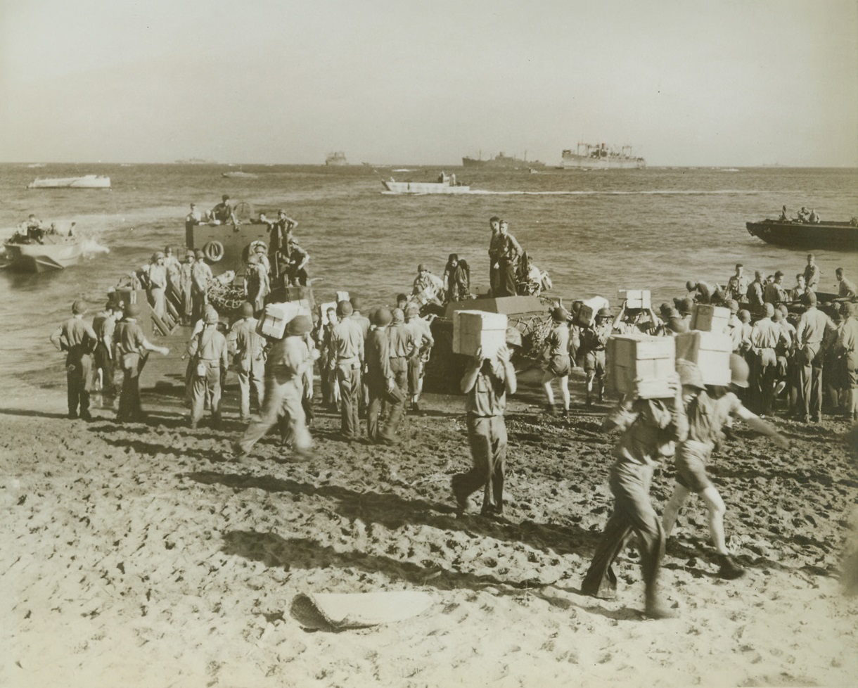Supplies for Marines on Guadalcanal, 12/29/1942. Guadalcanal – U.S. Marines unload supplies from small boats on the beach at Guadalcanal island.  In background, can be seen part of the convoy that brought the supplies to the fighting Leathernecks. Credit line (U.S. Marine Corps photo from ACME);