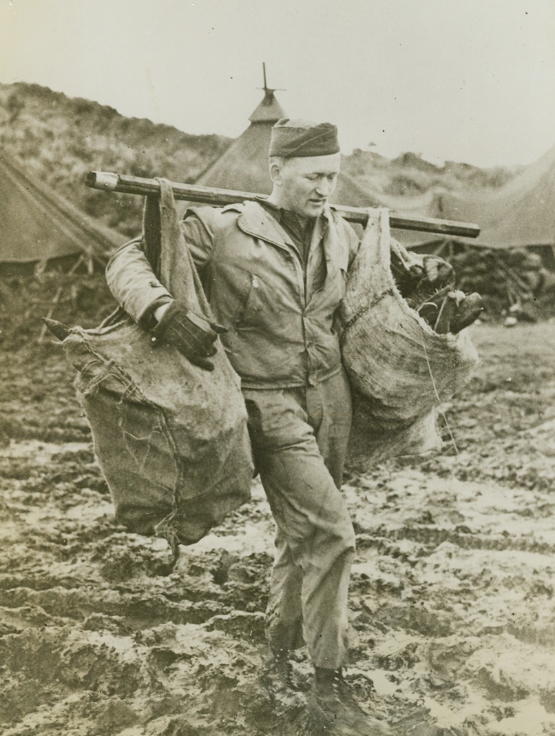 Aleutian Mud, 12/29/1942. The tasks of provisioning themselves and caring for their equipment sometimes proves as hard as smacking the Japs in fog-bound Kiska island nearby, but Uncle Sam’s flyers pitch right in.  The going was rather muddy for this soldier who’s carrying a supply of tent pegs over the soggy ground. Credit (Official Army photo – ACME);
