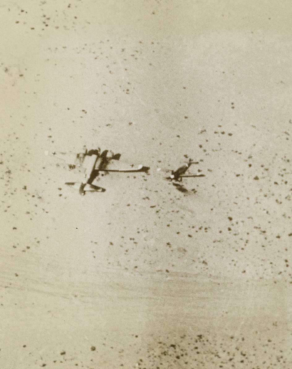Axis Warbirds Grounded, 12/5/1942. Libya—An Axis bomber and fighter plane were shot down side by side in the desert near Tobruk. Note tracks of land forces in the foreground. This photo was made from a U.S. plane on a mission near Tobruk.Credit: ACME.;
