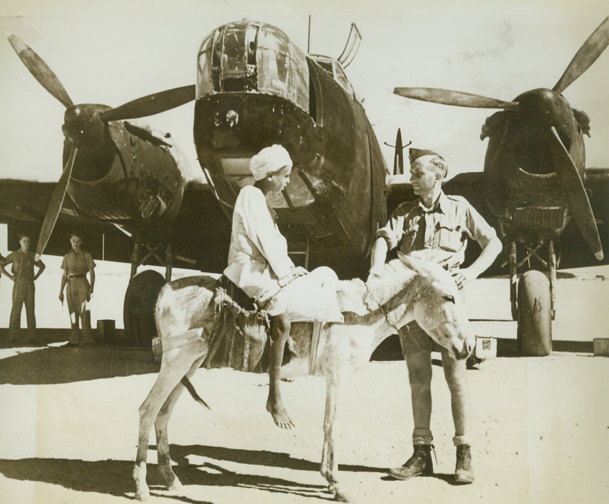 Old Meets New, 12/8/1942. Middle East—A native boy in the Middle East pays a call to an RAF pal at a desert airfield, his tiny donkey becomes even tinier when next to the giant Wellington bomber, but extremes in transportation are commonplace in this desert country where carts and camels jog along the same roads as streamlined automobiles and tanks.Credit: ACME.;