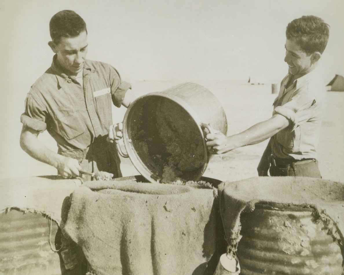Even in Africa, 12/8/1942. Western Desert—If Pvt. Frank Pauly (left), of Canton, Ohio, and Pvt. Louis Perrez, of Cotuela, Texas, had any idea they were going to get out of KP duty when they headed for Africa, they received an unwelcome surprise. But the two privates don’t seem to mind too much, as they roll up their sleeves and pitch in, at a Western desert bomber base.Credit: ACME.;