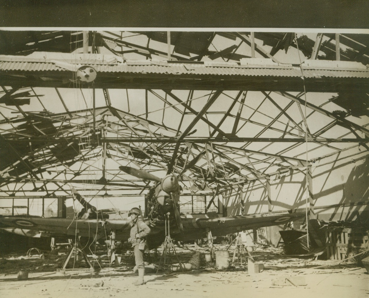 Americans on Duty in North Africa, 12/26/1942. An American soldier stands guard over a wrecked French plane beneath the skeleton of a hangar at “La Senia,” one of the principal airports captured by the United Nations near Oran. Passed by censor. Credit: ACME;
