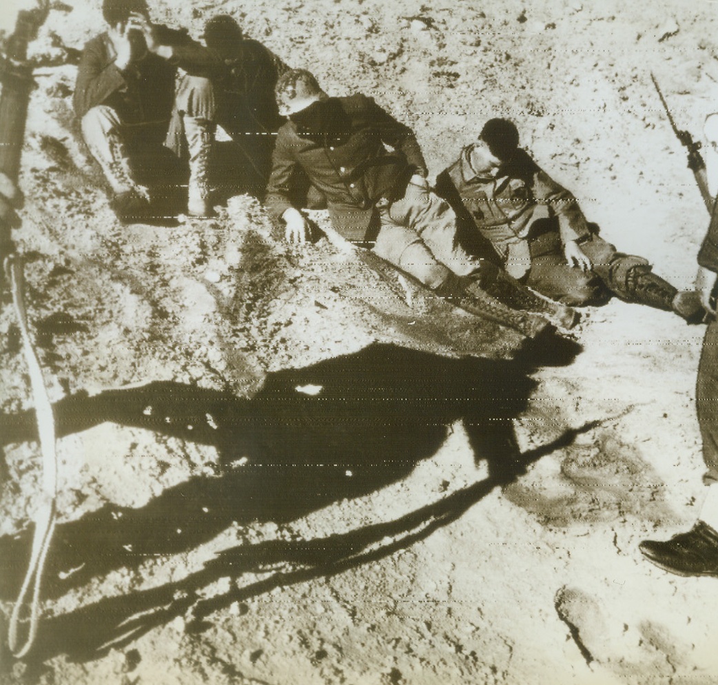 Shadowed by the Future, 12/28/1942. Western Desert—The shadow of an English guard is before these Nazi prisoners in a photo that is symbolic of the entire British advance in the desert where thousands of Nazis were rounded up. These spiritless Germans were captured after our Allies left Agheila and started toward Tripoli. The British are now only 180 miles from Tripoli where Rommel is moving the bulk of his army, 90 miles from the Eastern Tunisian border. Radioed from Cairo to N.Y. today. Credit: ACME radiophoto.;