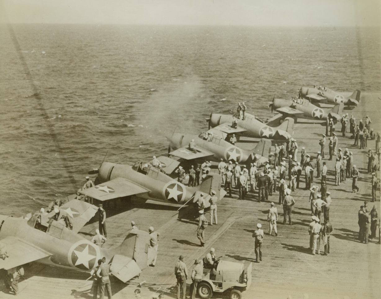 A Stitch in Time, 12/30/1942. Six U.S. Navy fighter planes line up on the side of a flight deck of an airplane carrier for machine gun firing, a precautionary check before beginning operations in North Africa. Credit: Official Navy photo, ACME.;
