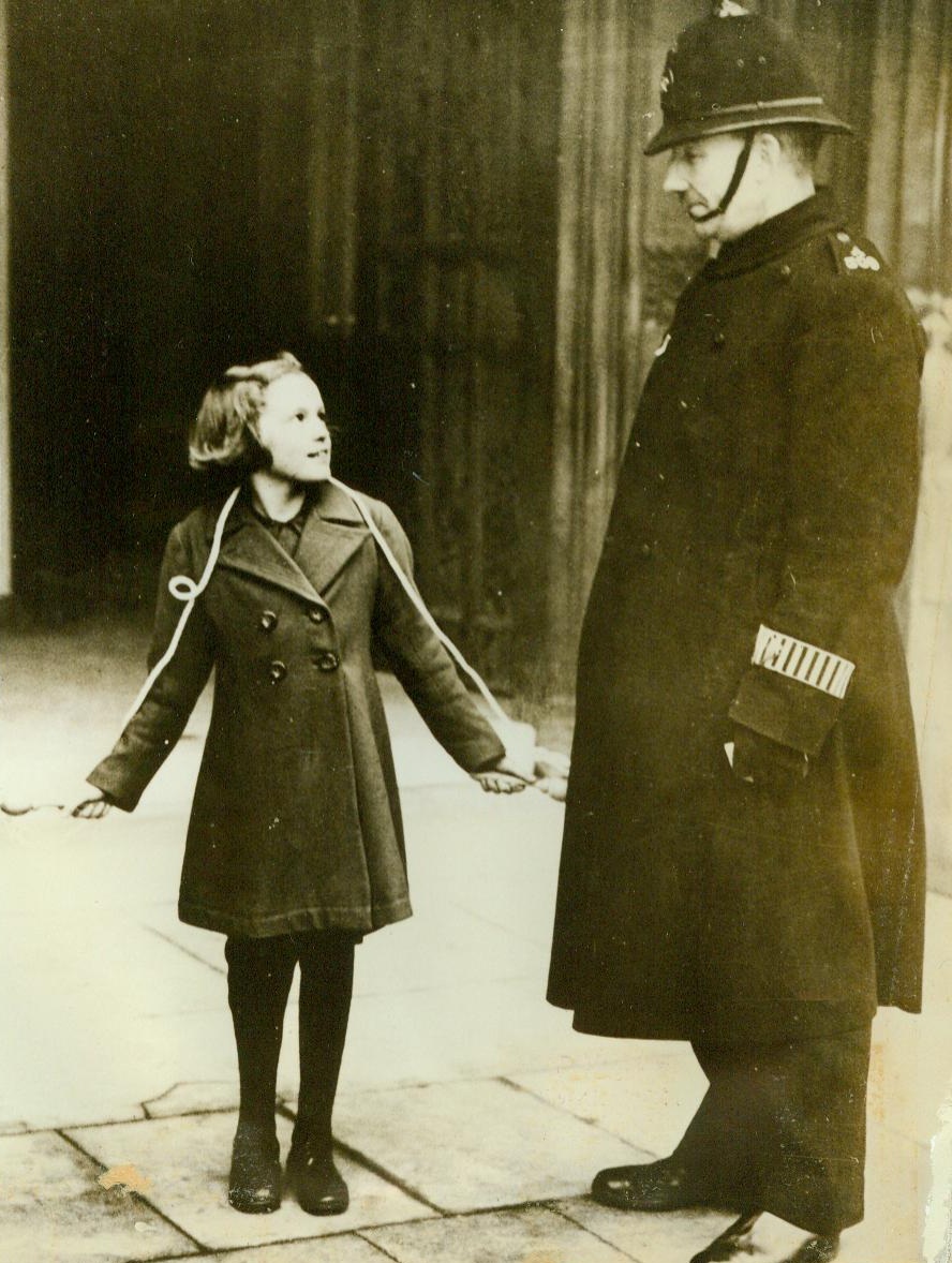 No Title. 12/2/1942. LONDON, ENGLAND - Little Joan Condon, a 12-year-old British schoolgirl, knows that "war is hell." A victim of an air raid, she lost her leg and had to get an artificial limb. The brave youngster overcame her disability and brought her skipping rope to the House of Commons to prove to members of that body that she is "just as good as new." She is shown outside the House, chatting with a London Bobby.;