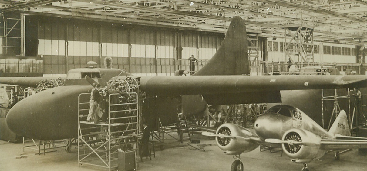 All-Wood Transport Plane, 12/12/1942. This is one of the first photos of America’s first all-wood military plane to be released. The plane, which is nearing completion at a plant of the Airplane Division of the Curtiss-Wright Corp. “somewhere in Missouri,” will undergo flight tests shortly. It will be used by the U.S. Army Air Forces to transport paratroops and air-borne troops to battle areas. Note how the Curtiss (C-76) Caravan dwarfs the Curtiss (At-9) Jeep beneath its wings in the foreground. Credit: ACME.;