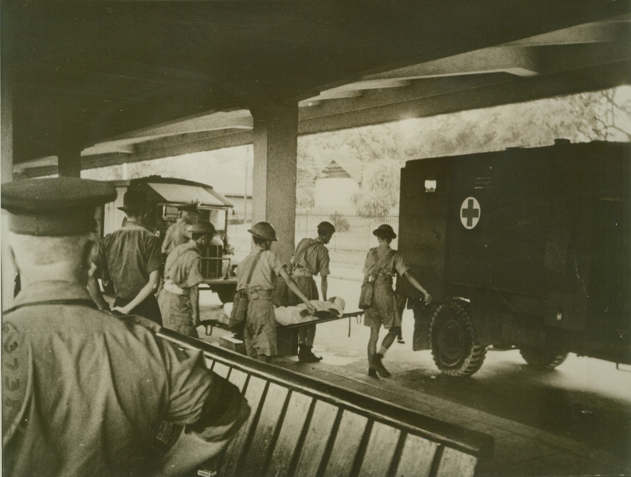 MALAYAN CHINESE HELP BRITISH WOUNDED, 2/11/1942. MALAYA – Chinese stretcher bearers carry a wounded British soldier to a waiting ambulance outside a Malayan station. Many Chinese served in this capacity during the Malayan campaign. Credit: ACME;