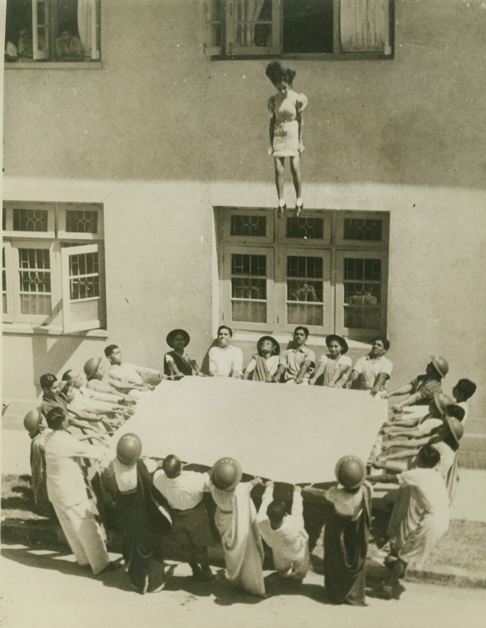 ALL INDIA JOINS IN DEFENSE, 2/13/1942. BOMBAY, INDIA – Realizing the nearness of the war to them, Indians are joining in an all-out effort to prepare for emergencies that might come. Just as in other countries, women, too, are training to do their part, and here a group of Parsee women, members of the ancient Zoroastrian sect, practice rescues that may follow air raids, in an A.R.P. class at the Cusrow Baug School. Credit: ACME;