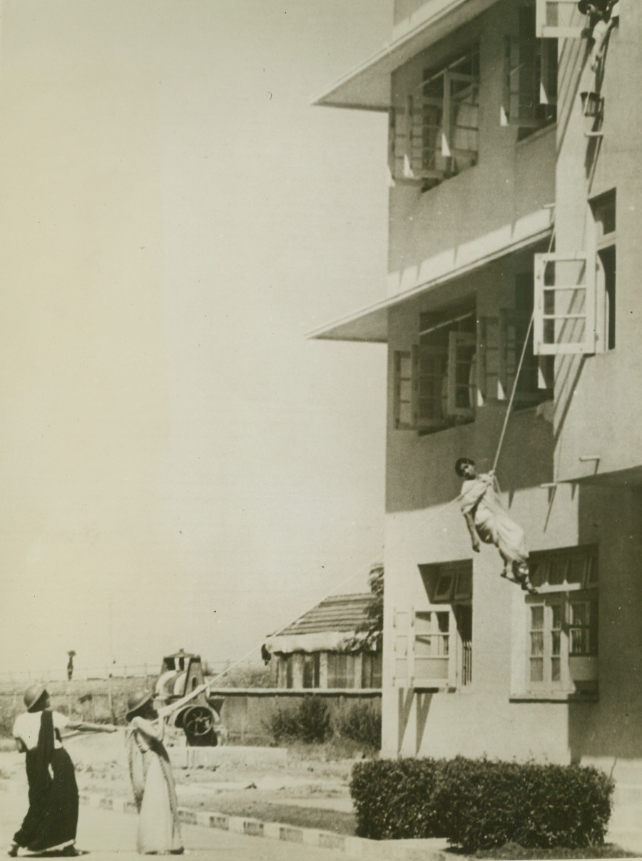 LL INDIA JOINS IN DEFENSE, 2/13/1942. BOMBAY, INDIA—Realizing the nearness of the war to them, Indians are joining in an all-out effort to prepare for emergencies that may come. Just as in other countries, women, too, are training to do their part, and here a group of Parsee women, members of the ancient Zoroastrian sect, practice lowering an air raid victim from a damaged building by means of a chair-knot. This method is only used when the fictim has not lost consciousness.Credit: Acme;