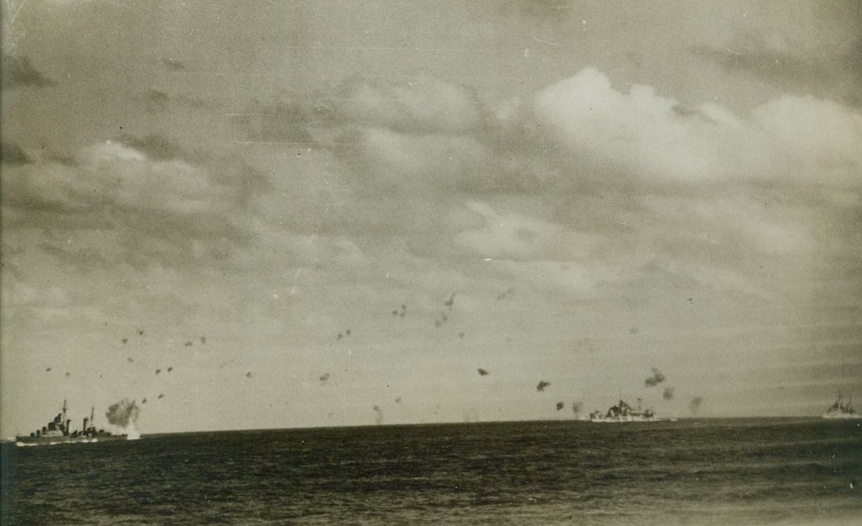 NEAR MISS IN AIR ATTACK ON BRITISH CONVOY, 2/28/1942. A bomb explodes dangerously near to the stern of a British destroyer (extreme left) escorting a convoy across the Mediterranean as a formation of over a hundred German and Italian planes blast away in a five-hour attack. A formidable barrage of anti-aircraft fire from the convoy’s escorting warships finally drove off the air attackers. One Italian torpedo bomber was shot down in flames. The convoy and its escort was undamaged. Credit: Acme;