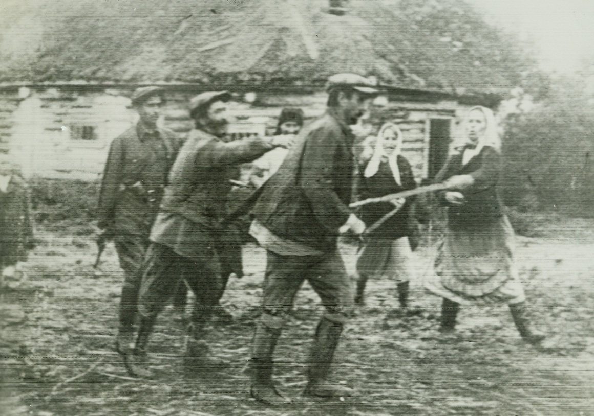 “March of Time”, 2/11/1942. No. 2 in series. Here the fifth columnist, foreground in cap, is led out after seizure by the men he betrayed. Women perhaps even the wives of the dead men, belabor the traitor with brooms and sticks.Credit: ACME telephoto;