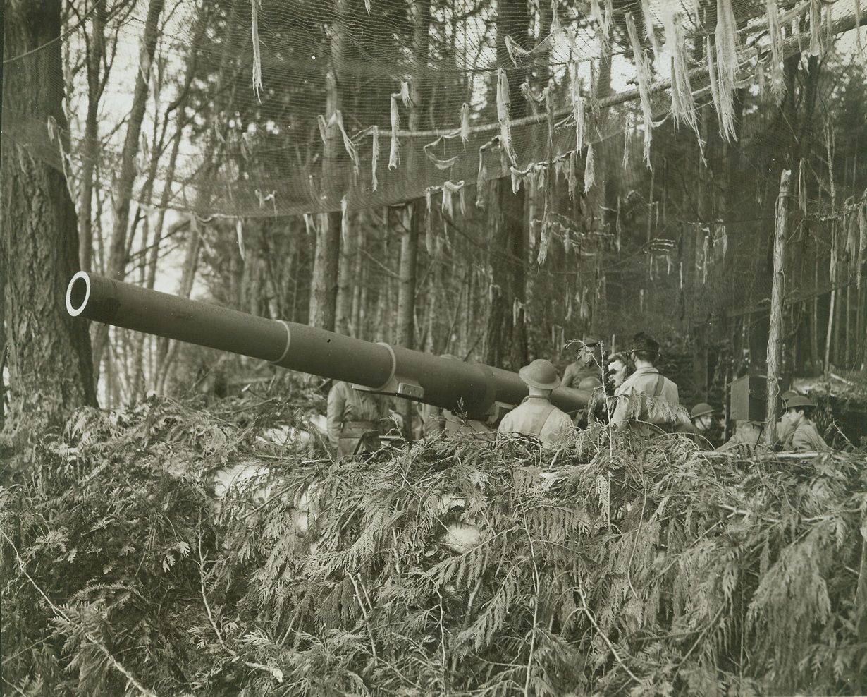 Seen Any “Visitors”?, 2/7/1942. One of the Army’s heavy mobile guns points out to sea somewhere in the Pacific Northwest from its camouflaged hiding place in the forest. Credit line (ACME);