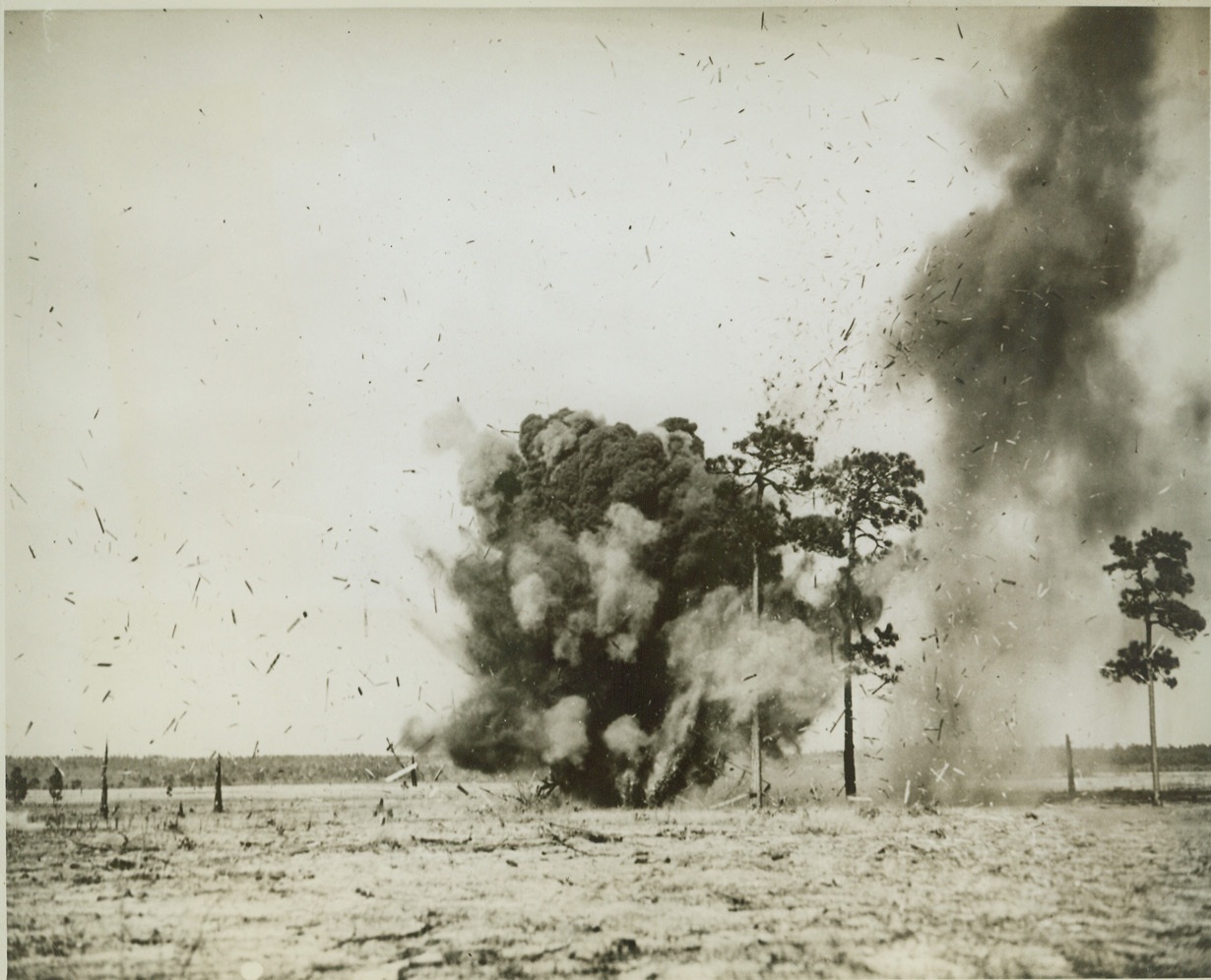 DIRECT HIT BY LONG-RANGE RIFLE, 3/29/1942. FORT BRAGG, N.C. – Debris flies in all directions as a shell from a 155mm Field Rifle scores a direct hit on a wooden shack during target practice by the 36th Field Artillery. The 155mm Rifle is the longest range – about 17 miles- field piece used by the U.S. Army Credit: OWI Radiophoto from ACME;