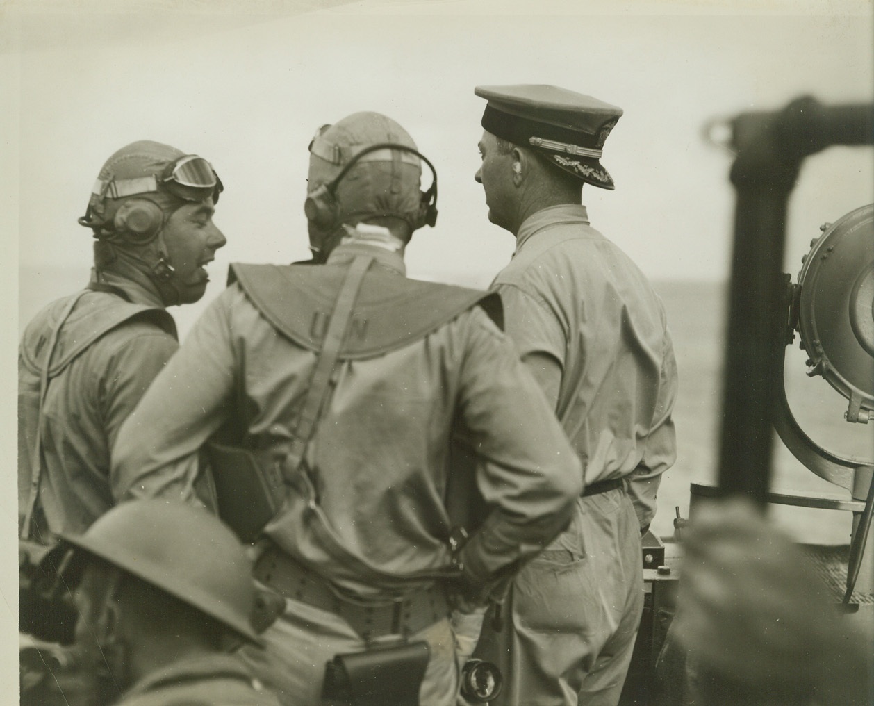 NAVY OFFICERS ON BRIDGE DURING CLASH WITH JAPS, 3/30/1942. SOMEWHERE IN THE PACIFIC – Officers on the bridge of a warship, part of a task force of the United States Pacific Fleet, during a hot engagement with Japs “somewhere in the Pacific.” Officer on right with his hat on backwards is captain of ship. Note cotton stuffed in his ears to protect them from injury during heavy gunfire. Two men on left are Navy fliers. Credit: ACME;